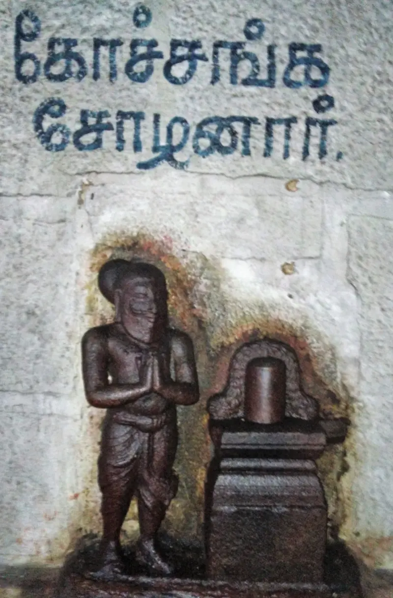 A dark stone carving of a praying king next to a small lingam, Tamil label above