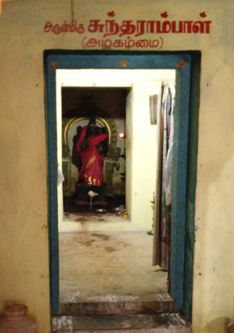 A doorway with a Tamil signboard, and a dark goddess figure in a red cloth inside