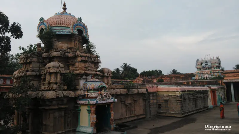 A tall carved stone tower with a painted dome beside a small porch, seen from the temple corridor.
