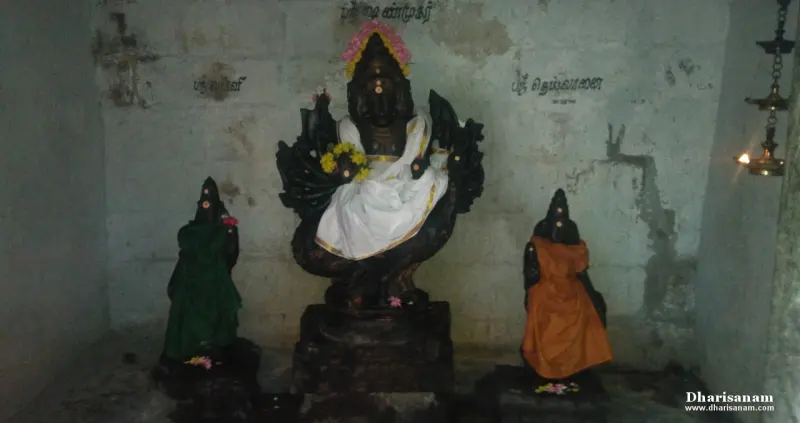 Three dark stone images stand on pedestals against a wall; the middle one wears white cloth.