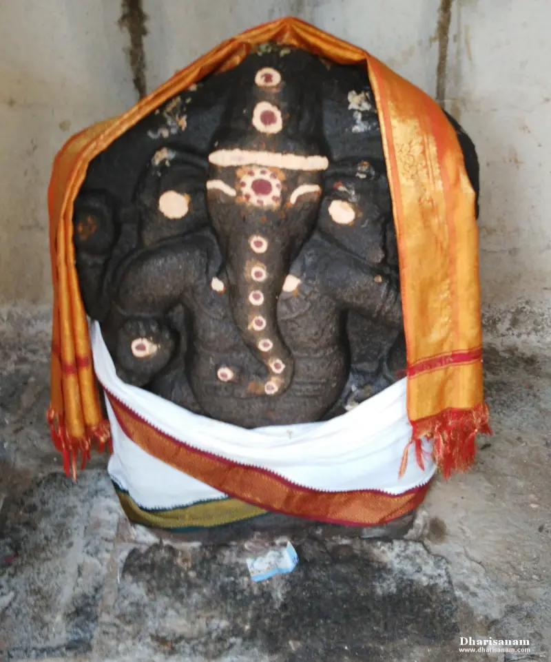 A dark stone idol of Vinayakar draped in an orange shawl and a white cloth, with sandalwood dots