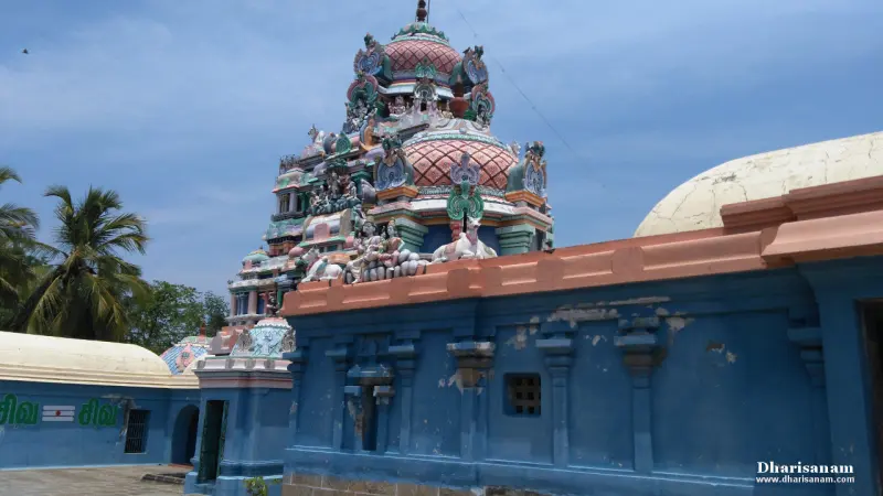 A painted tower with many sculptures rising over a blue wall, with a rounded roof to the right.