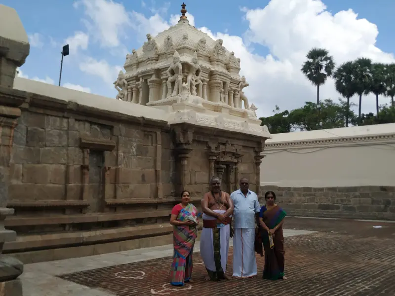 Four people stand before a stone shrine with a cream-coloured tower of sculpted figures, under a partly cloudy sky.