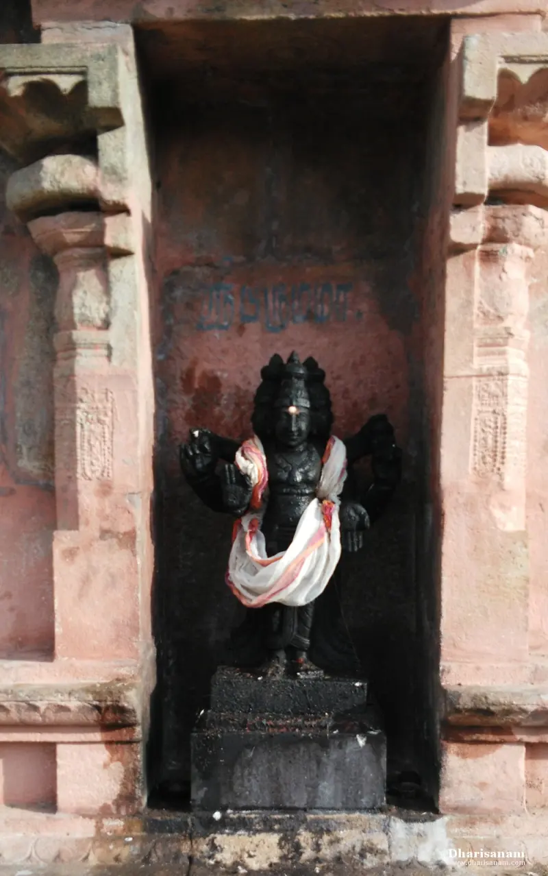 A dark four-armed idol in a draped cloth, standing in a stone niche.
