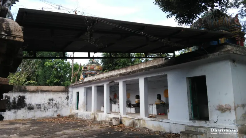 A whitewashed open hall with square pillars and idols on platforms inside, under a tin roof