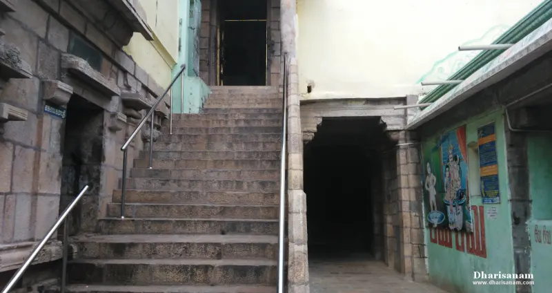 A wide flight of stone steps with metal railings between old stone walls, and a dark doorway at the right