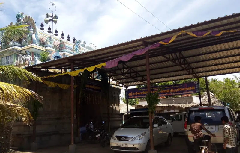 Tin-roofed shelter over the approach, with cars parked below and the temple tower behind