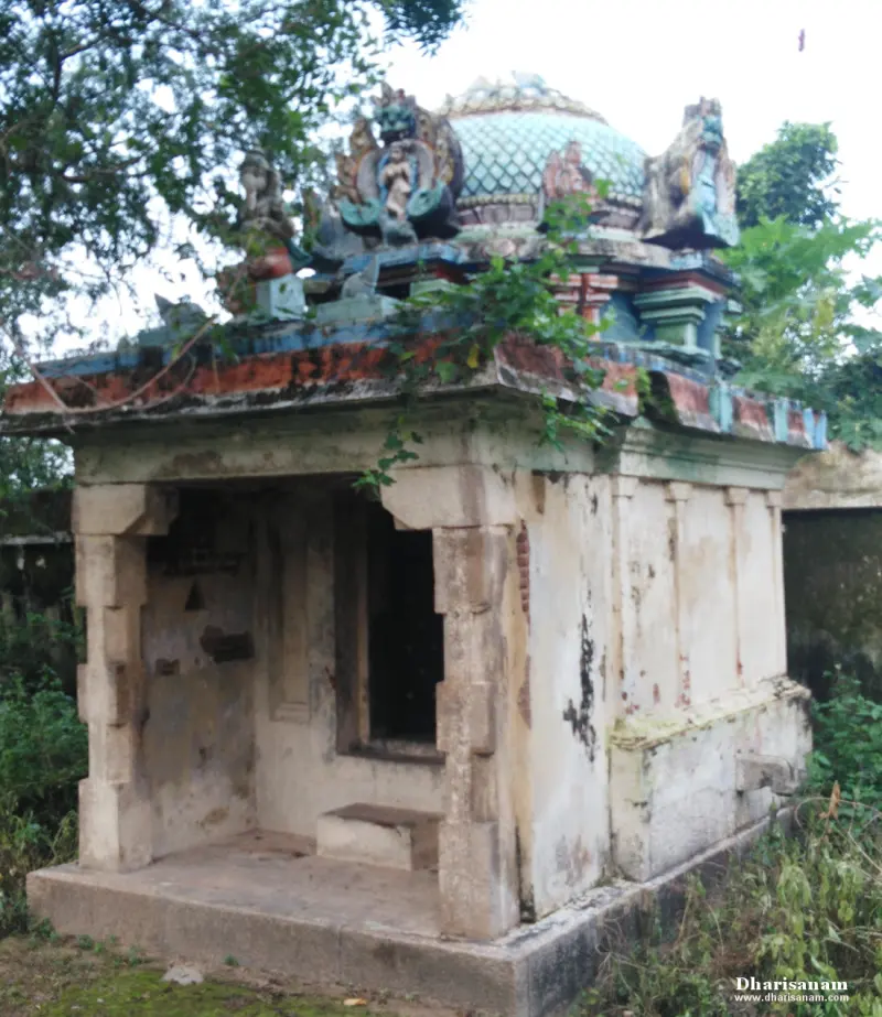 A small stone shrine with a painted dome and plaster figures on top, partly covered by creepers.