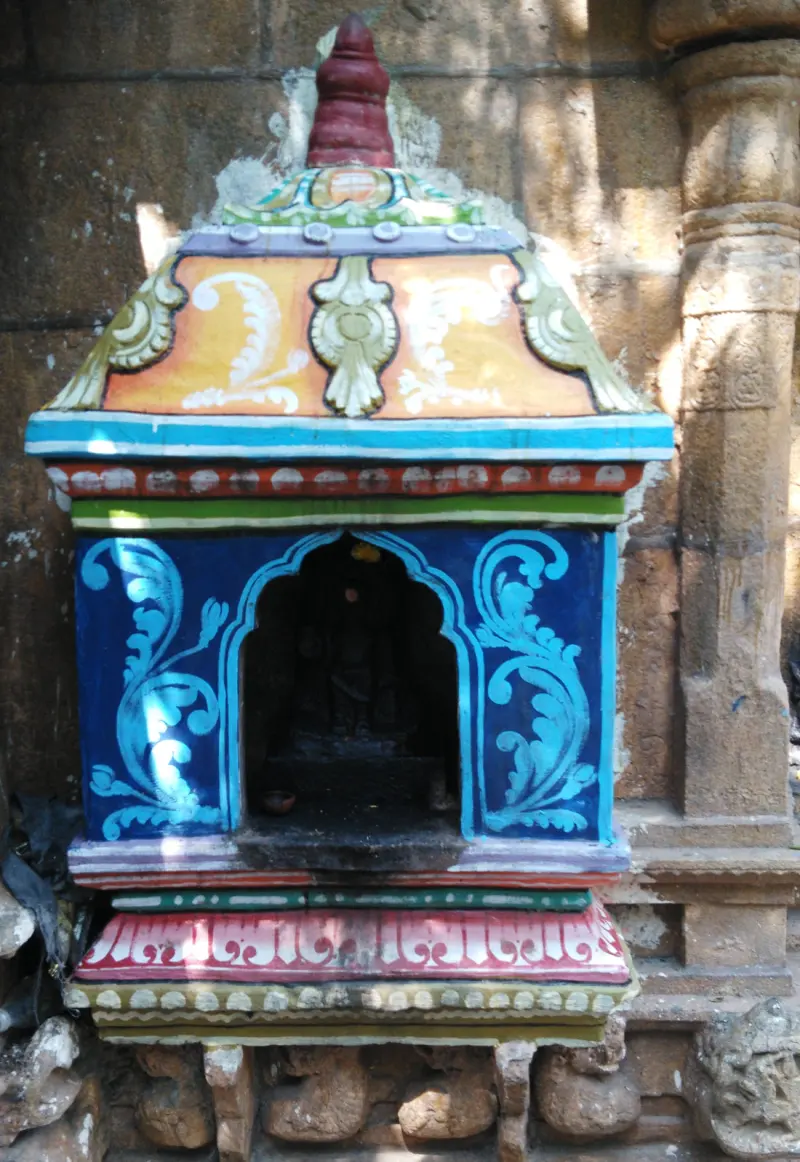 Small blue and orange painted shrine set against a stone wall, with a dark idol inside