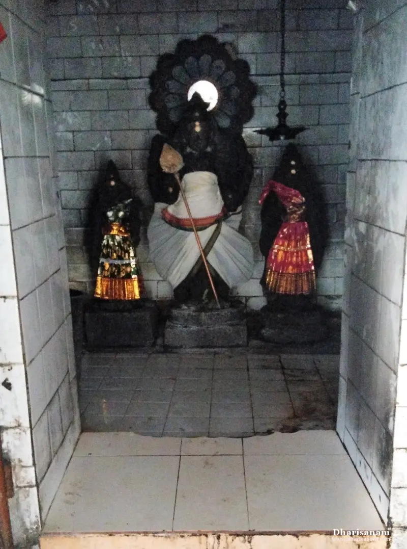 A dark stone deity in white cloth with a hood-like halo, flanked by two smaller dressed figures