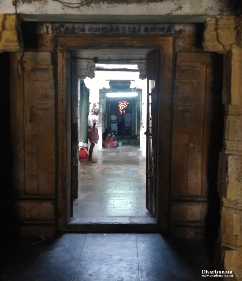 A dark stone doorway with a Tamil name board, a priest and a lamp-lit sanctum seen beyond