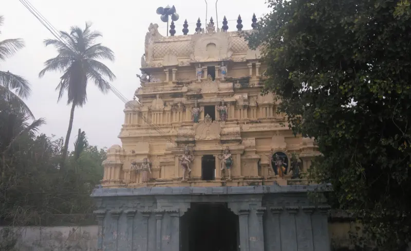 Front view of a three-tier gopuram covered in painted figures, a palm tree to the left