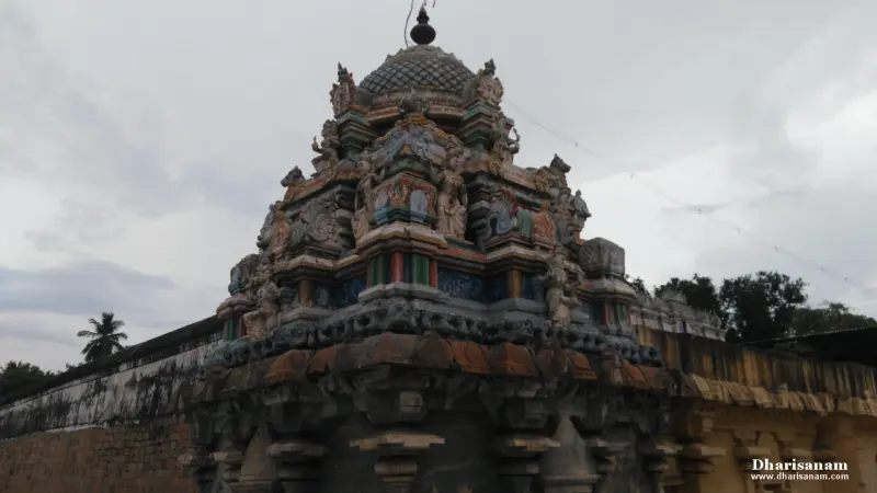 A colourful tower with many sculpted figures, rising above a stone wall under a grey sky.