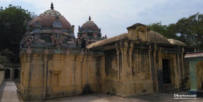 Old stone walls and weathered roofs of the sanctum beside two painted domed tower tops, under a grey sky