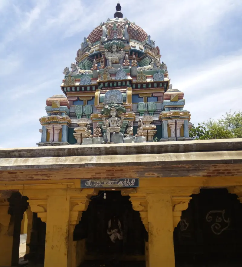 Yellow pillared porch under a Tamil name board, with a painted tower rising behind it