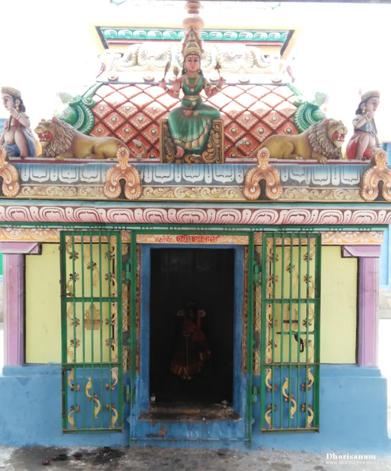 A small shrine with a painted goddess seated between two lions on its roof, and barred green gates.