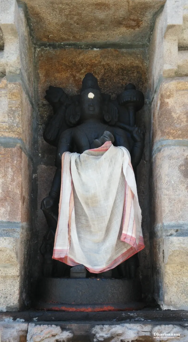 A dark stone idol with several arms, partly covered by a cream cloth, in a recess of the temple wall.