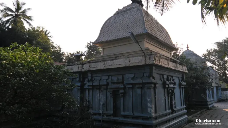 A grey stone shrine wall with carved bands and a sloping tiled roof, with leafy bushes in front