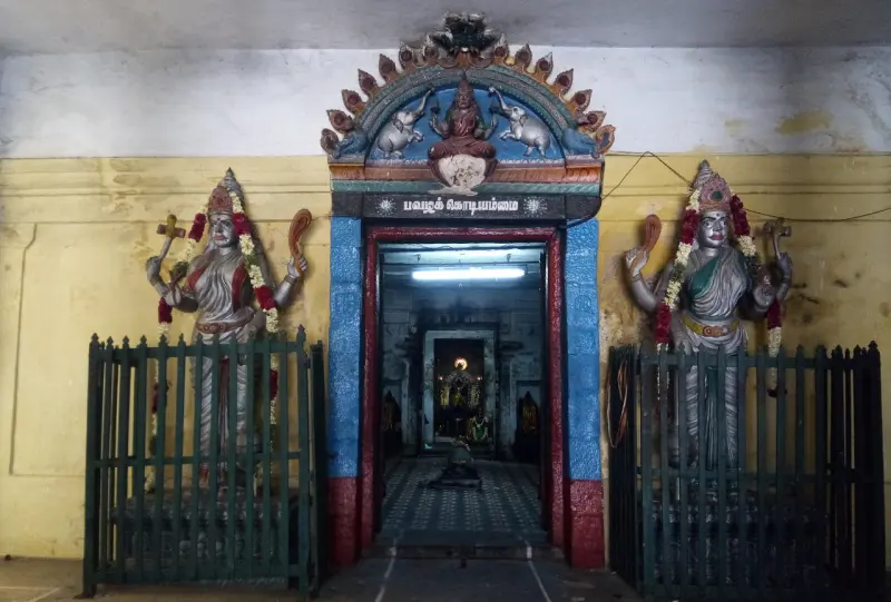 Painted figures stand at each side of a shrine doorway behind iron railings, with a seated figure above