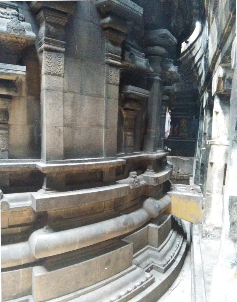 A dim passage beside a curved stone wall with carved pilasters and a rounded base moulding.