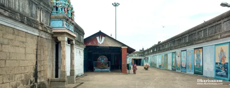 A paved corridor with a woman walking, a shrine with a Vishnu emblem ahead and painted panels on the right wall
