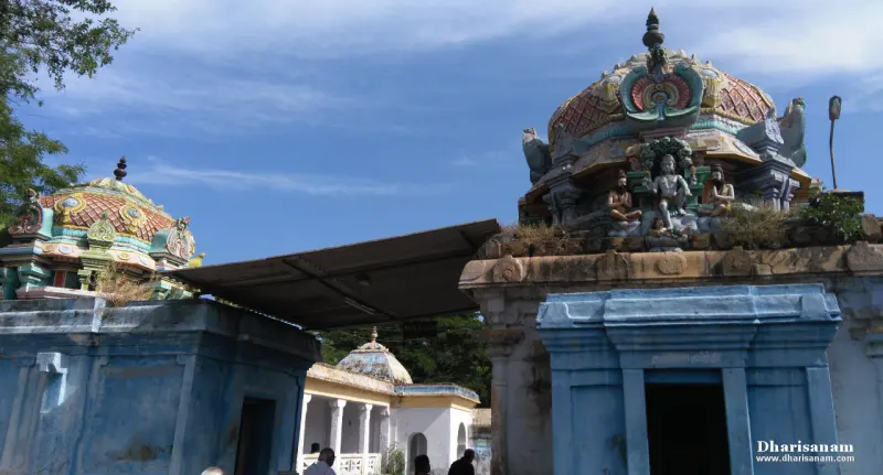 Blue shrines with painted domed roofs and a taller roof carrying figures, with a few visitors in the yard