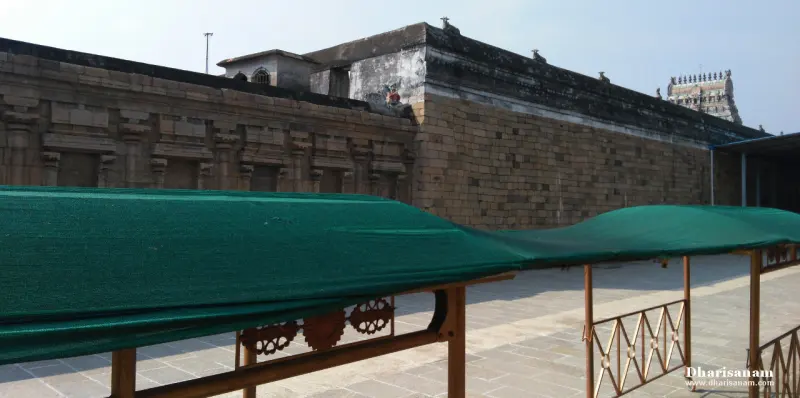 A long stone wall with a green shade over a metal walkway, a tower showing at the far right