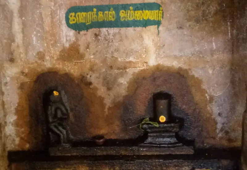 A small figure and a lingam in two arched recesses, under a green name board reading Karaikkal Ammaiyar
