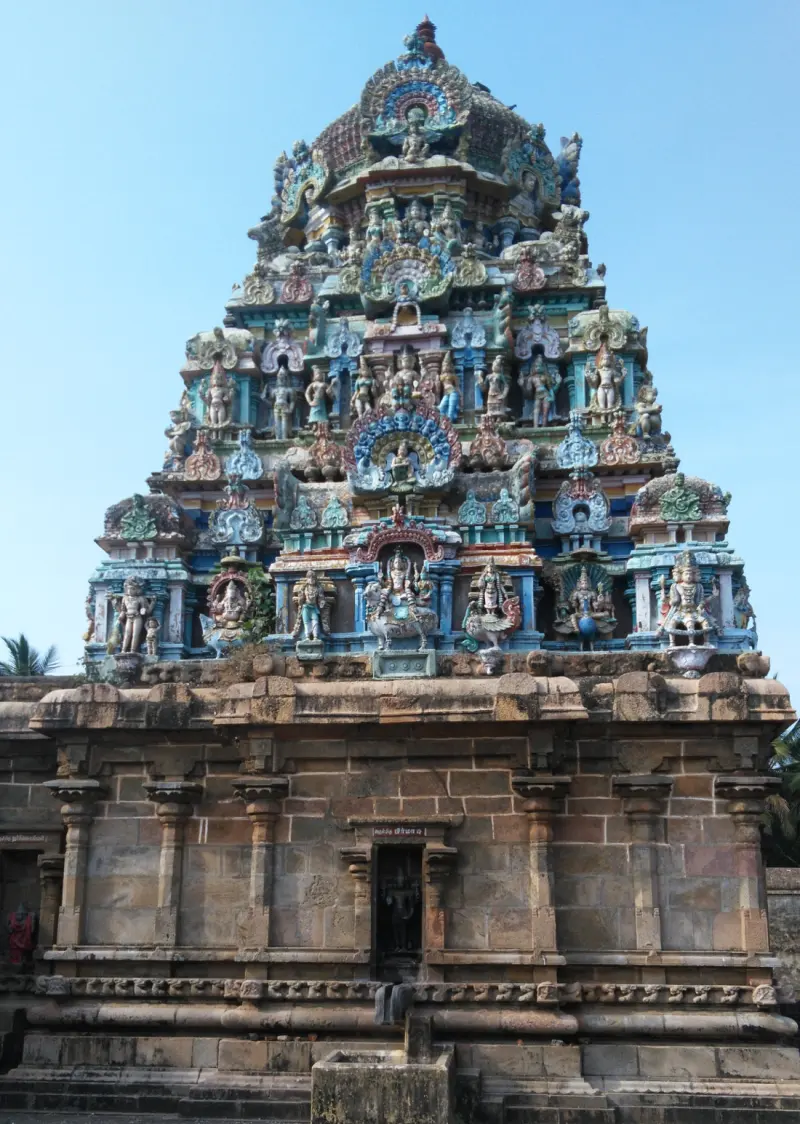 A tiered tower with painted figures on a plain stone base, seen against a blue sky