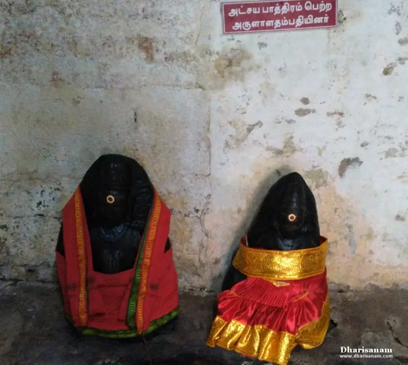 Two dark stone idols in red cloths with a board above them naming the couple who received the Akshaya Pathiram