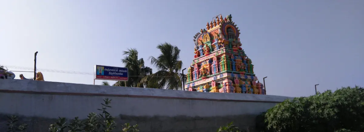 Colourful five-tier tower above a white wall, with palms and a signboard