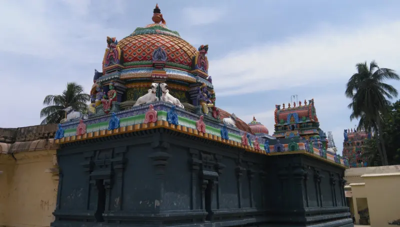 A dark stone shrine wall under a colourful dome with white bulls; towers rise behind