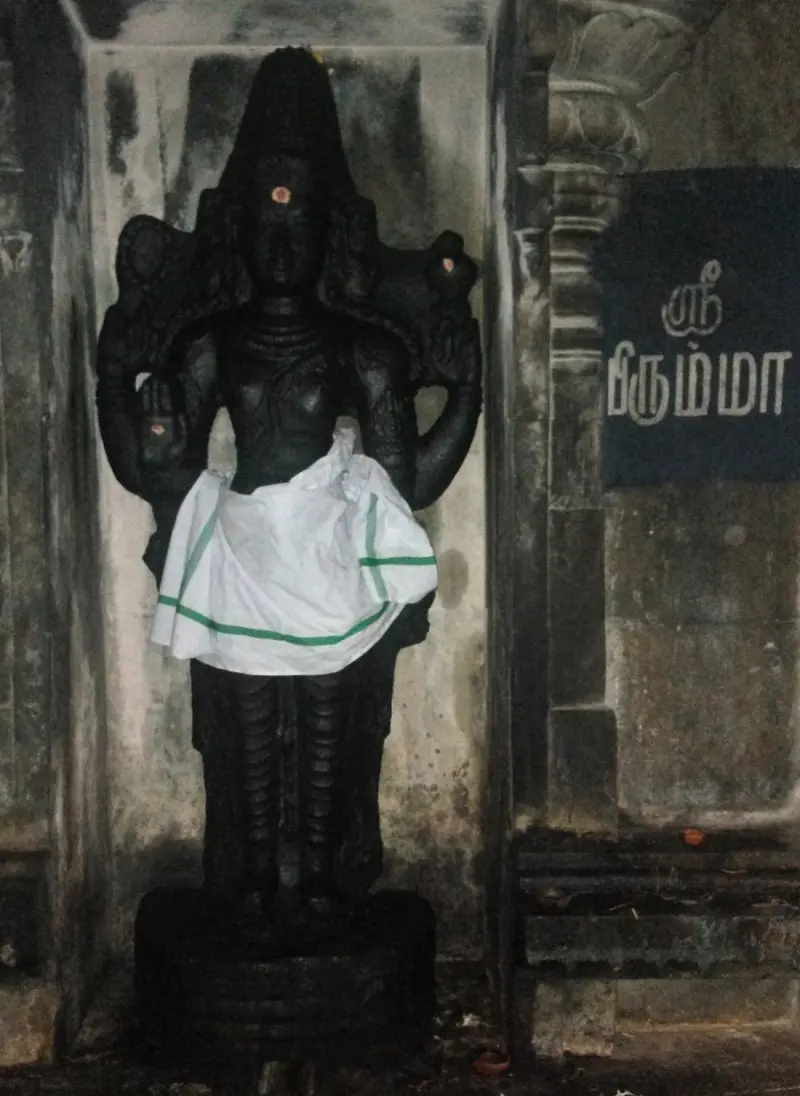 A dark standing figure with several arms in a niche, beside a Tamil name board