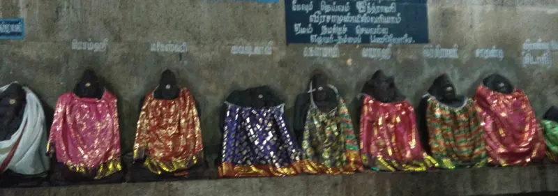 A row of small idols in coloured cloth along a wall