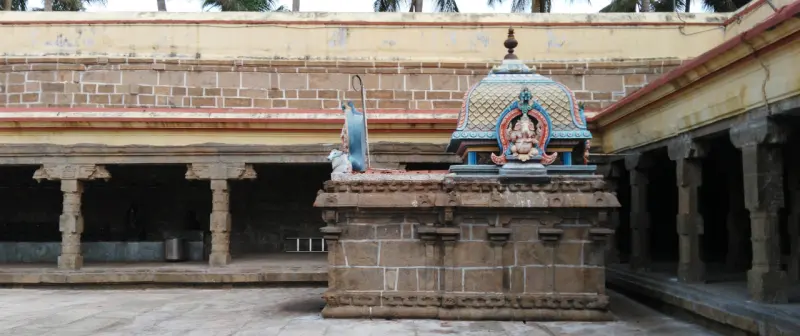 Stone shrine with a domed roof showing a Vinayakar figure, in front of a long pillared corridor