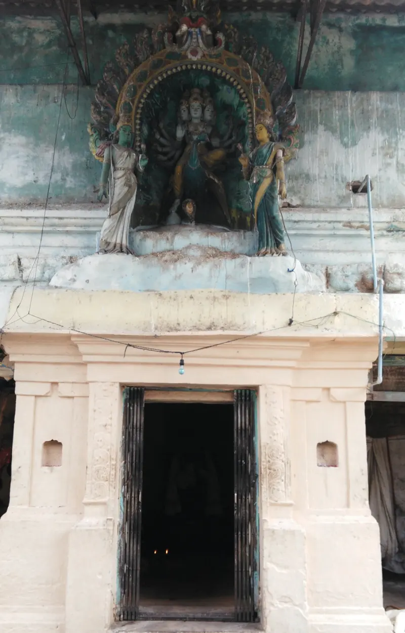 A cream-coloured shrine with iron gates; above it a painted arch holds a many-armed figure flanked by two women.