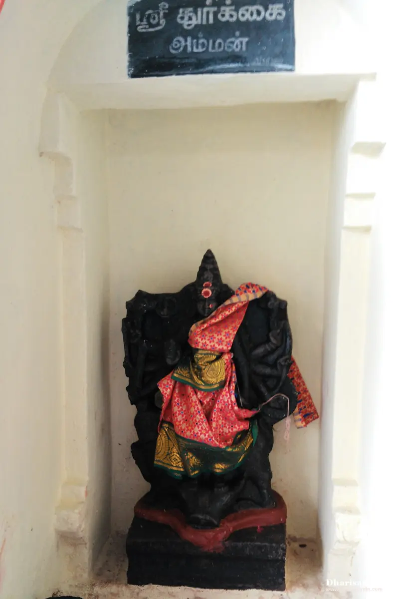 A dark many-armed image in red and green silk in a white niche under a Tamil name board
