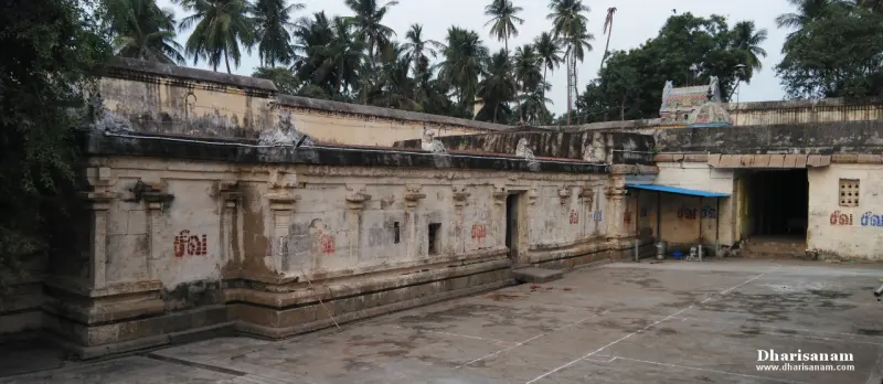 A long stone corridor wall with painted Tamil marks on it and a tiled passage entrance with palms behind