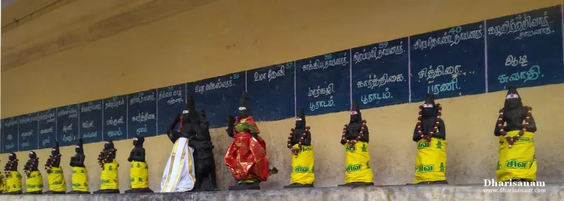 A long row of small dark idols in yellow cloth, each with a blue name board above it on the wall
