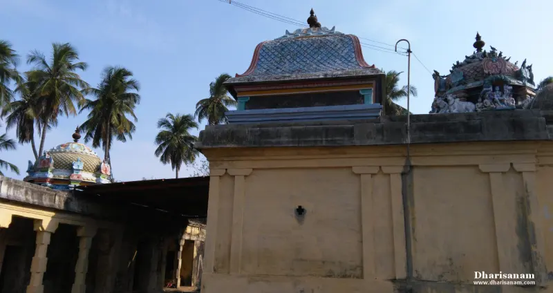 A yellow wall with a small tiled roof above it, and painted shrine roofs on both sides, palms behind