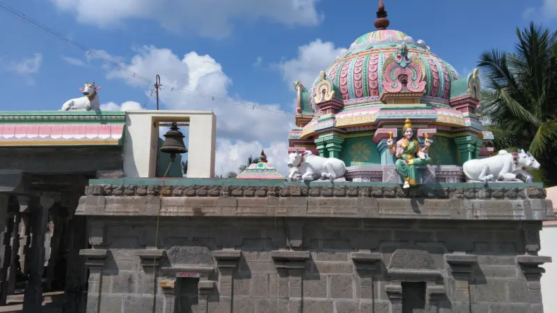 A green domed shrine roof with a stucco goddess and white bulls, and a hanging bell to the left