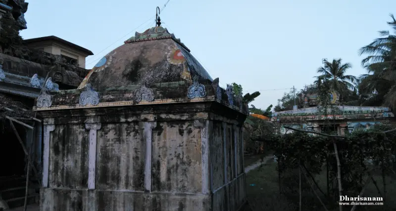 Small weathered shrine with a domed roof, trees and another shrine roof behind it under an evening sky
