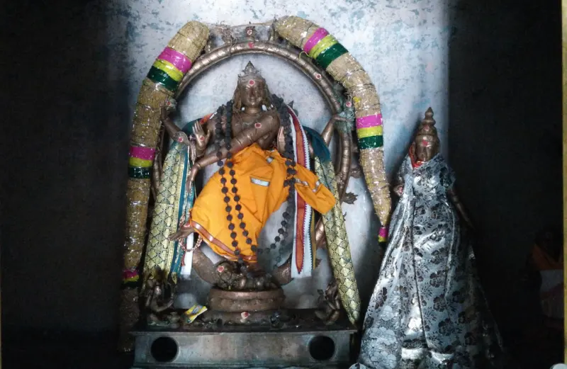 A bronze dancing figure in an orange cloth under an arch of garlands, with a draped image at the right.