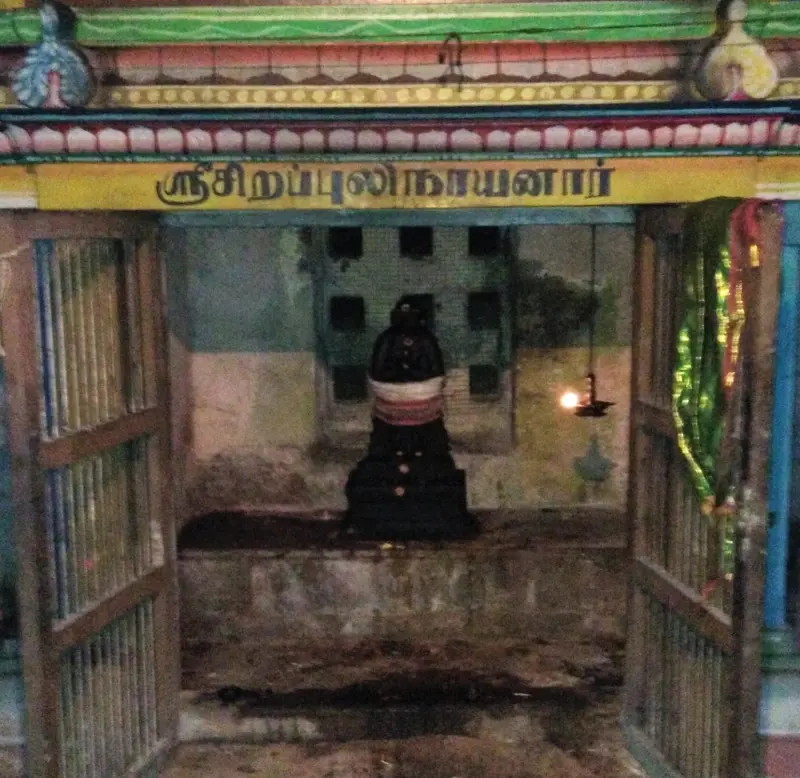 A small shrine with a dark idol and a hanging lamp under a Tamil name board