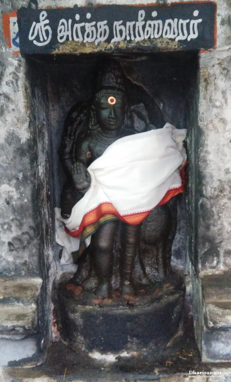 Black stone Arthanaareswarar standing in a niche under a name board, draped in white cloth