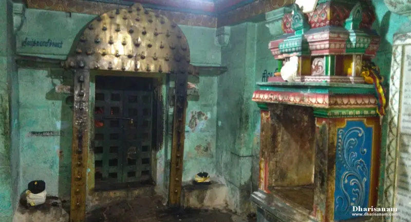 A studded wooden door in a green-walled passage, with a painted shrine front on the right