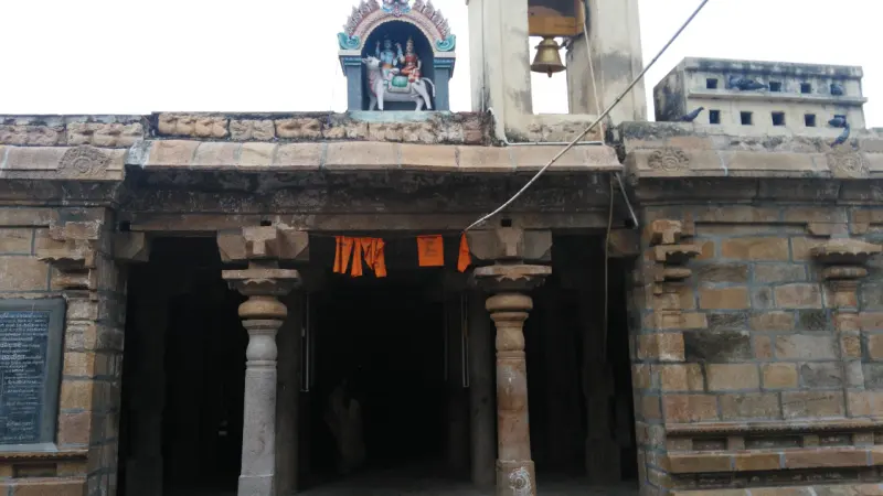 Stone porch with carved pillars, a hanging bell and a small painted figure above