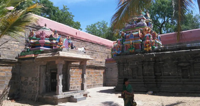 A small stone porch and a colourful tower behind a stone wall, with a woman walking in the foreground.