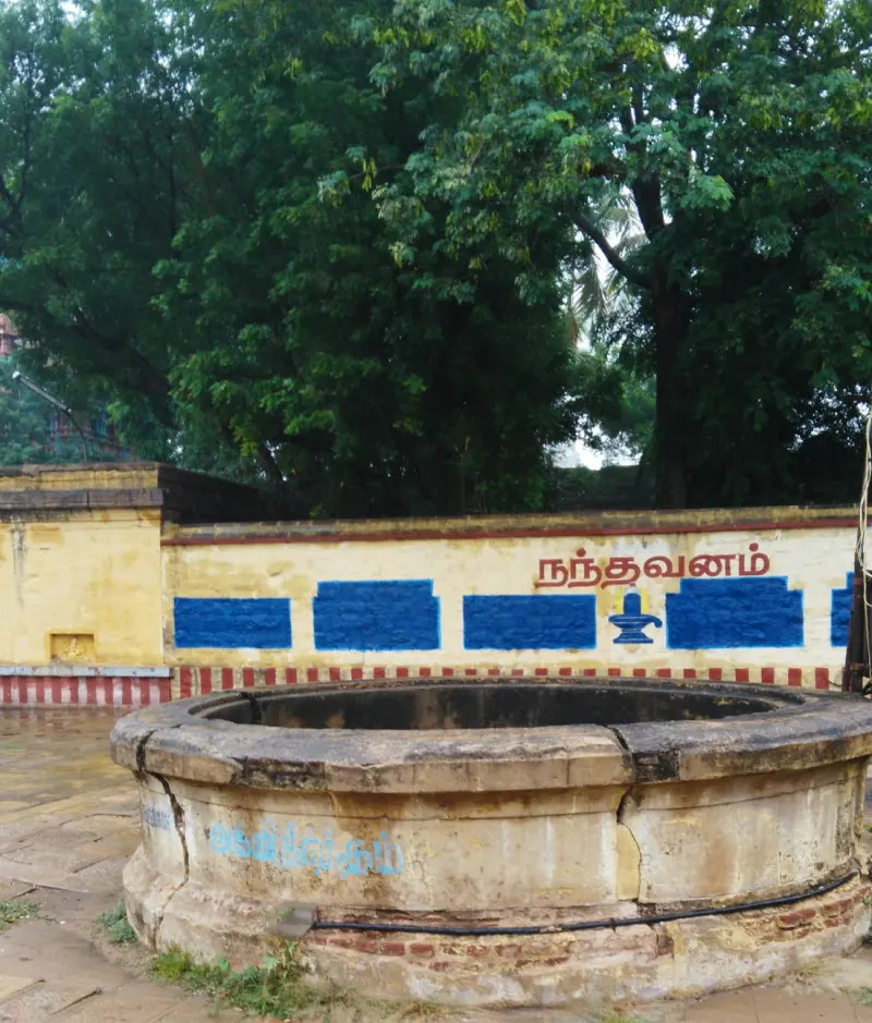 A round stone-rimmed well in front of a painted wall marked நந்தவனம், with trees behind.