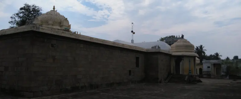 A tall dark stone wall with a domed roof at the far end, over a paved courtyard